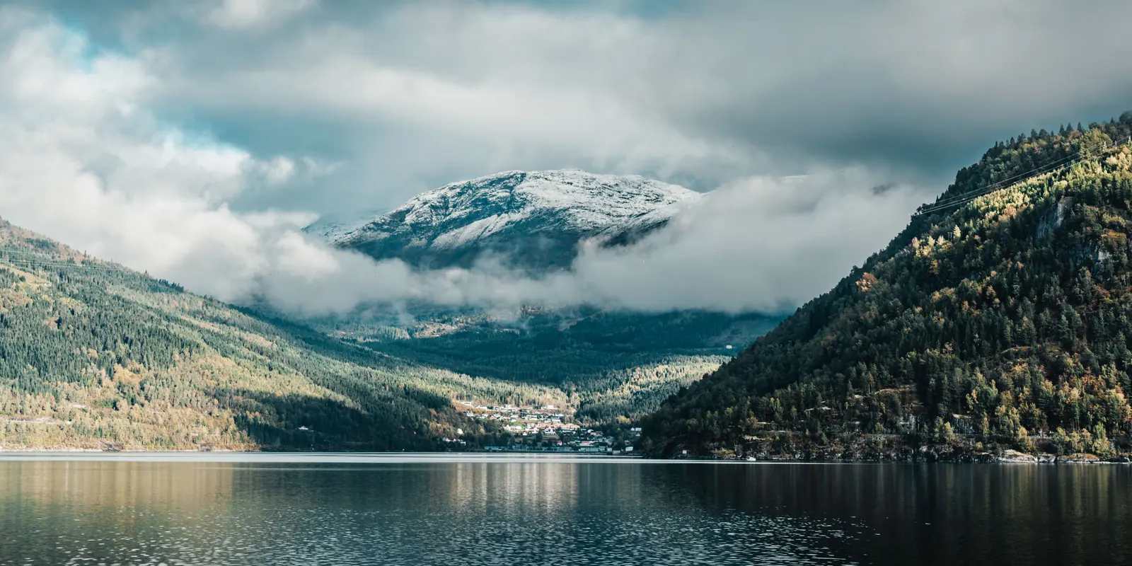 Fiordo con montaña nevada entre nubes